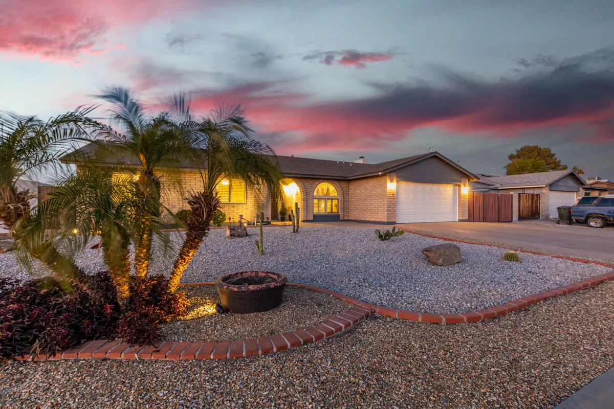 A serene exterior view showing palm trees, gravel landscaping, the home entrance, and a garage. The setting feels peaceful and inviting, highlighting the residential character and tropical landscaping.