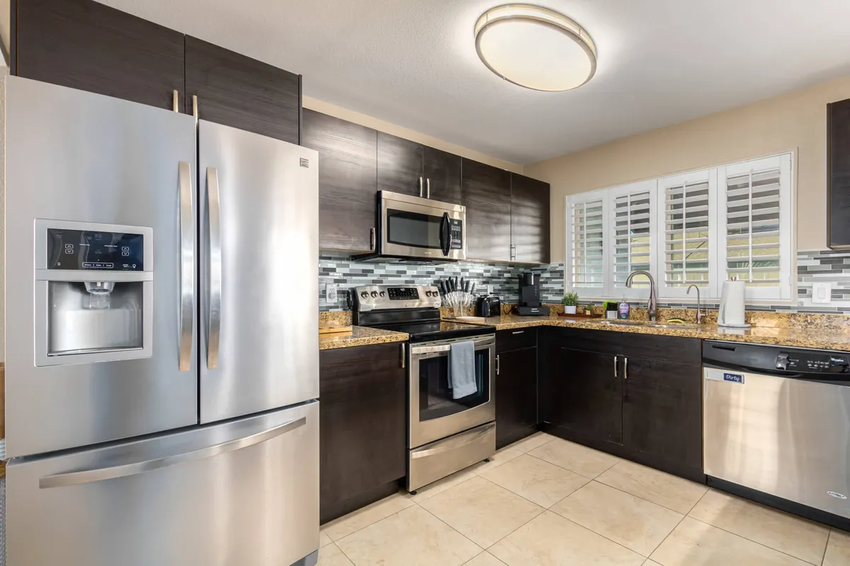 A bright, contemporary kitchen featuring stainless steel refrigerator and stove, granite countertops, and a stylish glass tile backsplash. The space feels open and inviting, with modern appliances and clean lines accented by subtle Southwestern-inspired decor elements.