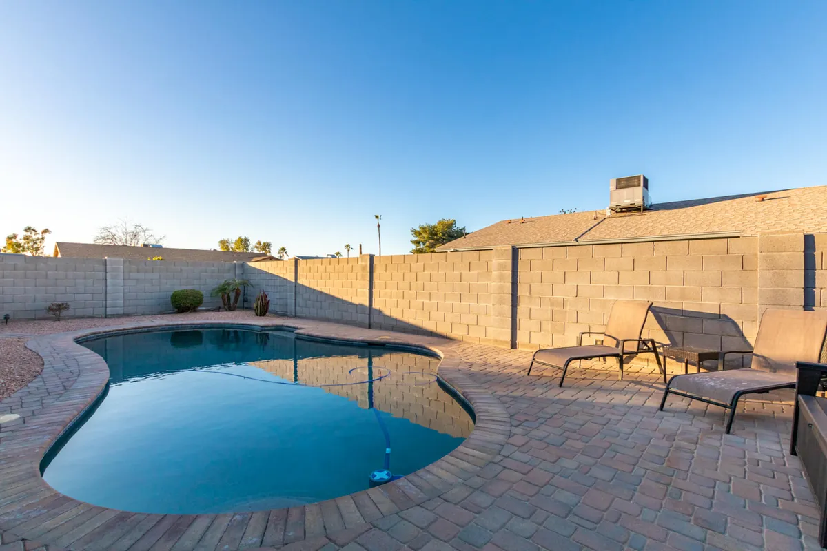 A bright, sunlit pool area outfitted with lounge chairs and shielded by surrounding walls and palm trees. The setup is designed for both swimming and socializing, offering privacy and a resort-like feel.