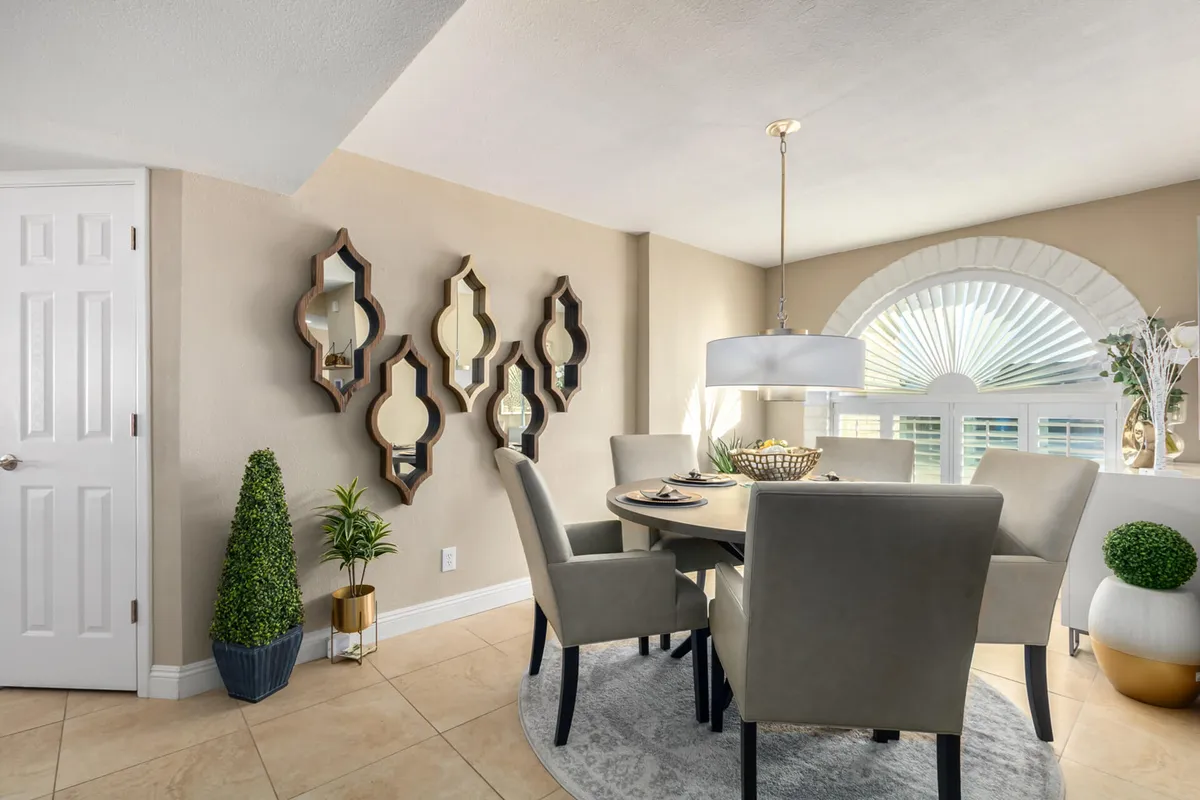 A dining area bathed in warm sunlight, featuring a large dining table, decorative mirrors on the wall, elegant window treatments, and lush potted plants. The setting feels both vibrant and comfortable, ideal for family meals or extended conversations after a day of activities.