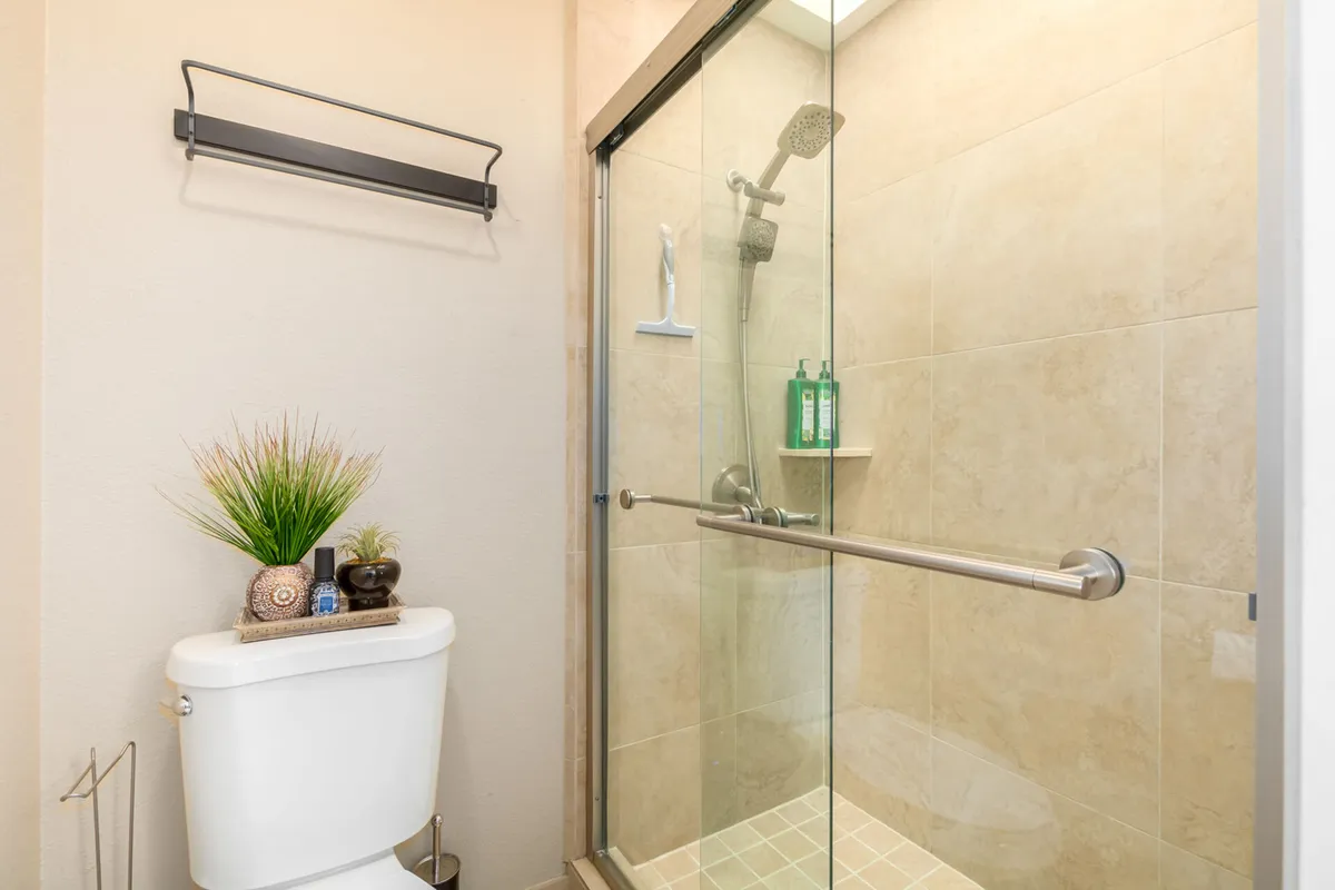 A bright, modern bathroom featuring a glass shower enclosure, a toilet, and a decorative plant adding a touch of freshness. Clean lines and natural light create a tranquil space for relaxation and rejuvenation.